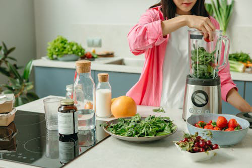 A person adding vegetables to a blender for a smoothie