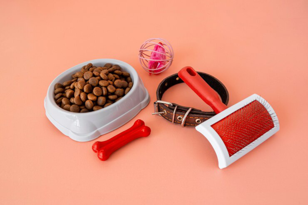  A set of dog accessories, including a food bowl and grooming brush, on a wooden surface