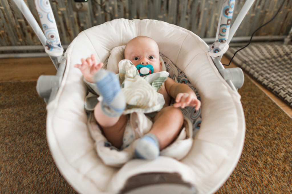 An infant lying in a moveable bassinet at home, sucking on a pacifier and looking relaxed