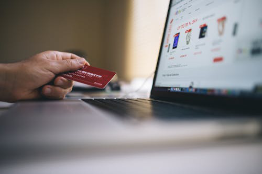 A hand holding a credit card while shopping on an online platform open on a laptop screen