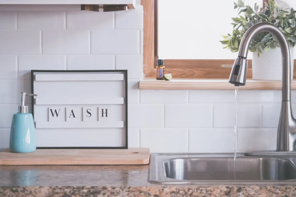 A modern bathroom faucet with running water beside a glass soap dispenser