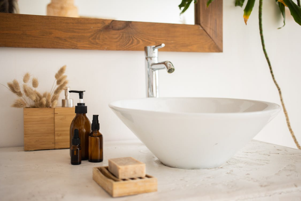 A sink styled with glass bottles of soap and cosmetic oil beside a matching lotion dispenser set
