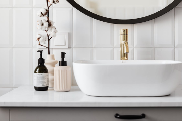 A white ceramic sink cluttered with bottles featuring various product labels