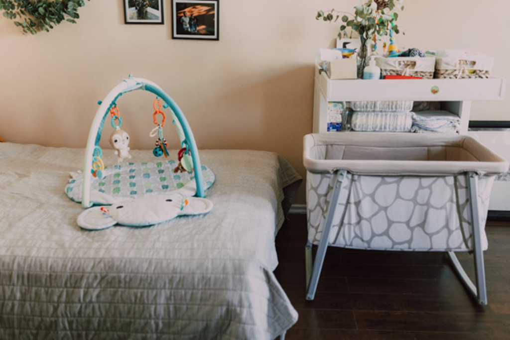 A nursery with a moveable bassinet and play gym next to a diaper changing station