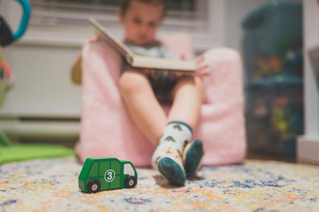 a child seated reading in a reading nook with toys