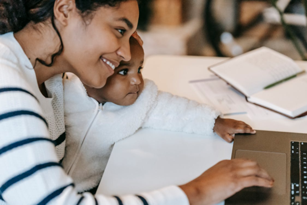 A smiling mother and baby looking at a laptop together.